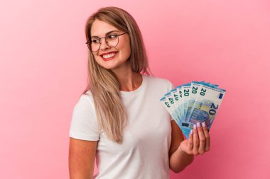Pembe arka planda izole edilmiş banknotları tutan genç Rus kadın gülümseyen, neşeli ve keyifli görünüyor..