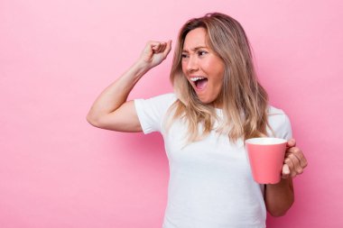 Pembe arka planda izole edilmiş pembe kupa tutan genç Avustralyalı kadın zaferden sonra yumruğunu kaldırıyor, kazanan konsept..