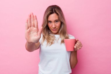 Pembe arka planda izole edilmiş pembe bir kupa tutan genç Avustralyalı kadın elini uzatıp dur işareti göstererek seni engelliyor..