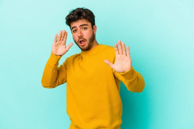 Mavi arka planda izole genç beyaz adam yakın bir tehlike nedeniyle şoka uğruyor