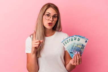 Pembe arka planda izole edilmiş banknotlar tutan genç Rus kadının harika bir fikri var, yaratıcılık kavramı..