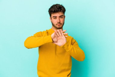 Kafkasyalı genç adam mavi arka planda izole edilmiş bir şekilde inkar hareketi yapıyor.