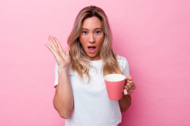 Pembe kupa tutan genç Avustralyalı kadın. Pembe arka planda izole edilmiş. Şaşırmış ve şok olmuş..
