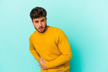 Mavi arka planda karaciğer ağrısı çeken, karnı ağrıyan genç beyaz bir adam..