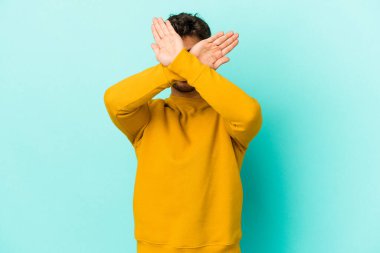 Kafkasyalı genç adam mavi arka planda izole edilmiş iki kolu çapraz tutuyor, inkar kavramı.