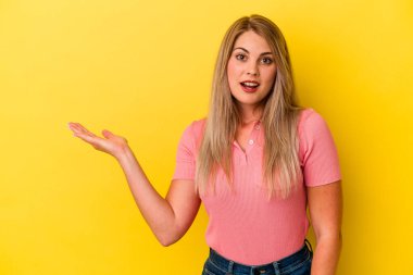 Sarı arka planda izole edilmiş genç Rus kadın, avuç içi fotokopi alanını elinde tutmaktan etkilenmiş..