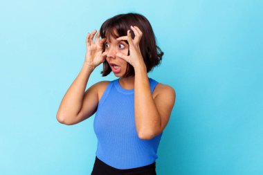 Mavi arka planda izole edilmiş genç melez kadın bir başarı fırsatı bulmak için gözlerini açık tutuyor..