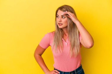Genç Rus kadın sarı arka planda izole edilmiş, uzaklara bakıyor ve elini alnına koyuyor..
