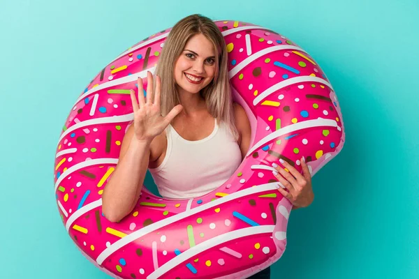 Şişme donutlu genç Rus kadın mavi arka planda izole edildi. Beş numarayı parmaklarıyla gülümseyerek gösteriyor..