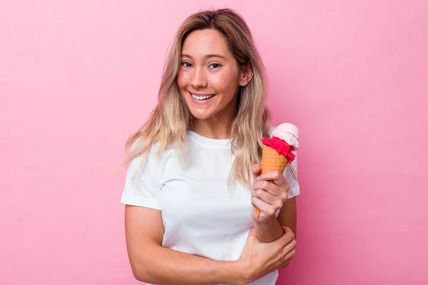 若いオーストラリア人女性がピンクの背景に孤立したアイスクリームを持って笑って楽しい — ストック写真