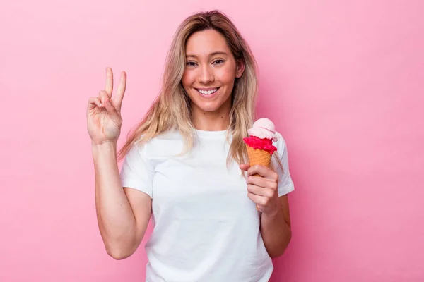 拿着用粉红背景隔开的冰淇淋的年轻的澳大利亚女人用手指显示了二号 — 图库照片