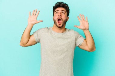 Kafkasyalı genç adam mavi arka planda izole edilmiş gökyüzüne haykırıyor, yukarı bakıyor, hayal kırıklığına uğramış..