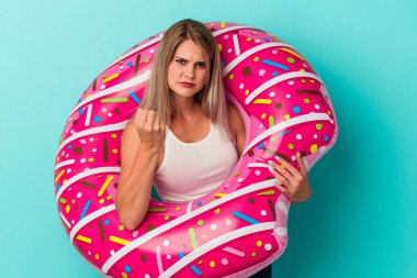 Mavi arka planda izole edilmiş şişme donutlu genç Rus kadın kameraya yumruğunu gösteriyor, agresif yüz ifadesi var..