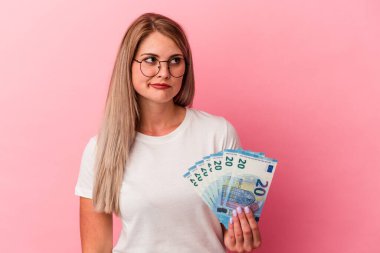 Pembe arka planda izole edilmiş banknotları tutan genç Rus kadın kafası karışmış, şüpheli ve güvensiz hissediyor..