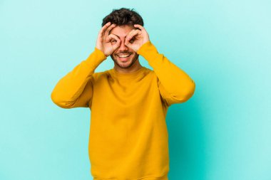 Mavi arka planda izole edilmiş genç beyaz adam gözlerinde sorun olmadığını gösteriyor.