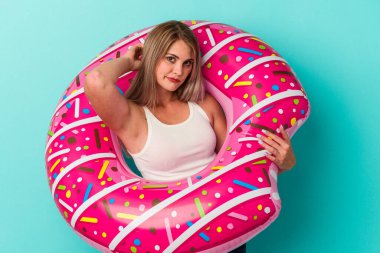 Şişme donutlu genç Rus kadın mavi arka planda izole edilmiş kafasının arkasına dokunuyor, düşünüyor ve bir seçim yapıyor..