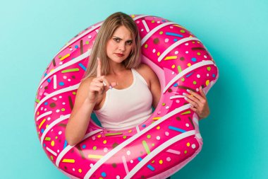 Şişme donutlu genç bir Rus kadın mavi arka planda izole edilmiş ve parmağıyla bir numarayı gösteriyor..