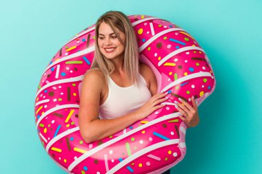 Mavi arka planda izole edilmiş şişme donutlu genç Rus kadın gülümsüyor, neşeli ve keyifli görünüyor..