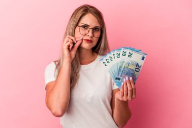 Genç Rus kadın pembe arka planda izole edilmiş banknotlar tutuyor parmakları dudaklarında bir sır saklıyor.