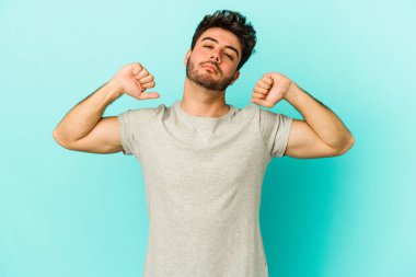Mavi arka planda izole edilmiş genç beyaz adam kollarını uzatıyor, rahat bir konumda..