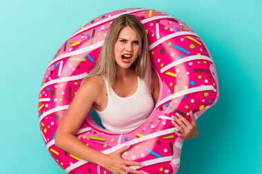 Şişme donutlu genç Rus kadın mavi arka planda izole edilmiş çok kızgın ve agresif çığlıklar atıyor..