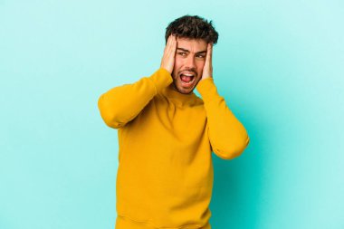 Kafkasyalı genç adam mavi arka planda izole edilmiş kulakları kulaklarıyla kapatıyor çok fazla ses duymamaya çalışıyor..