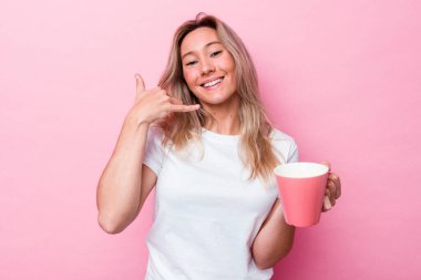 Pembe arka planda pembe kupa tutan genç Avustralyalı kadın parmaklarıyla bir cep telefonu hareketi gösteriyor..