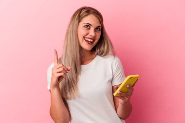 Elinde cep telefonu olan genç bir Rus kadın pembe arka planda izole edilmiş ve ağzı açık bir şekilde üst tarafı işaret ediyor..