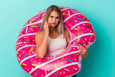 Şişme donutu olan genç bir Rus kadın mavi arka planda izole edilmiş ve parmakları dudaklarında bir sır saklıyor..