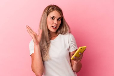 Elinde cep telefonu olan genç bir Rus kadın pembe arka planda izole edilmiş, şaşırmış ve şok olmuş..