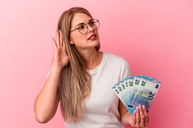 Pembe arka planda izole edilmiş banknotları tutan genç Rus kadın bir dedikoduyu dinlemeye çalışıyor..