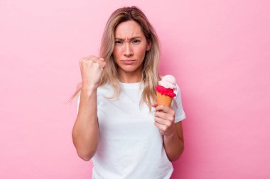 Elinde dondurma tutan genç Avustralyalı kadın pembe arka planda izole edilmiş yumruğunu kameraya gösteriyor, agresif bir yüz ifadesi var..