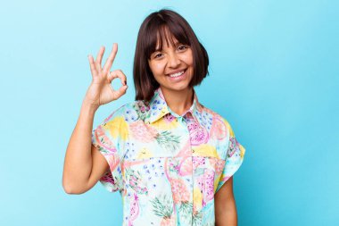 Mavi arka planda soyutlanmış genç melez bir kadın bir göz kırptı ve elleriyle iyi bir jest yaptı..