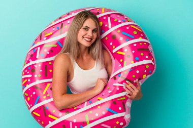 Şişme donutlu genç Rus kadın mavi arka planda izole edilmiş gülüyor ve eğleniyor..