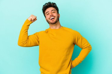 Kafkasyalı genç adam mavi arka planda izole edilmiş kaygısız ve heyecanlı tezahüratlar yapıyor. Zafer konsepti.