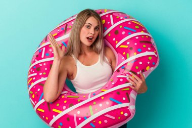 Şişme donutlu genç Rus kadın mavi arka planda izole edilmiş, şaşırmış ve şok olmuş..