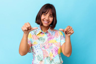 Mavi arka planda izole edilmiş genç bir ırk kadını iki parmağını da kaldırıyor, gülümsüyor ve kendinden emin..