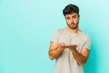 Kafkasyalı genç adam mavi arka planda izole edilmiş dudaklar kıvrılıyor ve hava öpücüğü göndermek için avuç içleri tutuyor..
