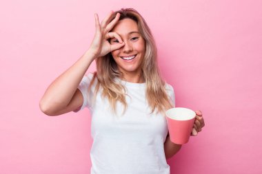 Genç Avustralyalı bir kadın pembe bir kupa tutuyor. Pembe arka planda izole edilmiş. Heyecanlı..