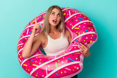 Şişme donutu olan genç bir Rus kadın mavi arka planda izole edilmiş, ağzı açık, üst tarafı işaret ediyor..