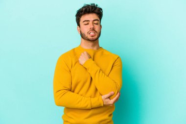 Kafkasyalı genç adam mavi arka planda izole edilmiş dirsek masajı yapıyor, kötü bir hareketin ardından acı çekiyor..