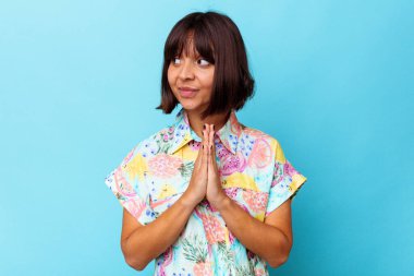 Genç melez kadın mavi arka planda izole edilmiş dua ediyor, bağlılık gösteriyor, dindar biri ilahi ilham arıyor..