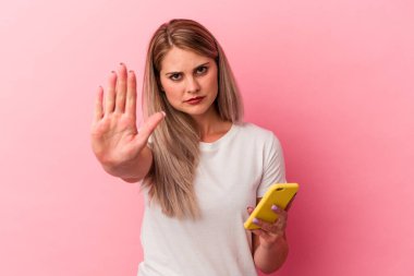 Pembe arka planda izole edilmiş cep telefonu tutan genç Rus kadın elini uzatıp dur işaretini göstererek seni engelliyor..