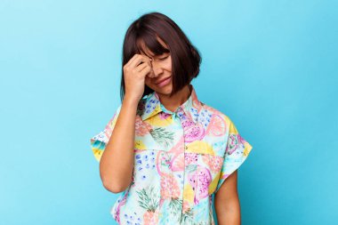 Genç melez kadın mavi arka planda izole edilmiş, başı ağrıyor, yüzüne dokunuyor..
