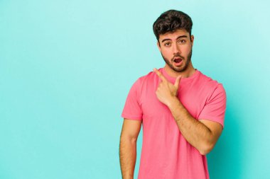 Mavi arka planda izole edilmiş genç beyaz adam yan tarafı işaret ediyor.