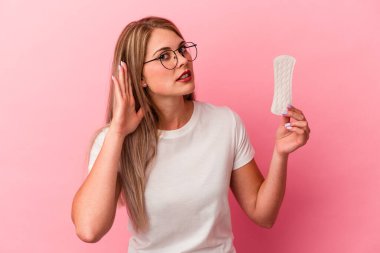 Pembe arka planda bir kompres tutan genç Rus kadın bir dedikoduyu dinlemeye çalışıyor..