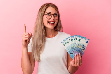 Elinde pembe arka planda izole edilmiş banknotlar tutan genç Rus kadın ağzı açık bir şekilde üst tarafı işaret ediyor..
