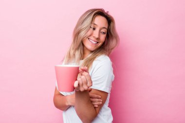 Pembe arka planda pembe kupa tutan genç Avustralyalı kadın gülümsüyor, neşeli ve keyifli görünüyor..