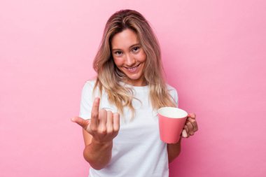 Genç Avustralyalı bir kadın pembe bir kupa tutuyor. Pembe arka planda izole edilmiş. Seni işaret ediyor..