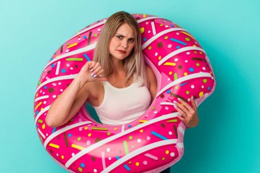 Şişme donutlu genç Rus kadın mavi arka planda izole edilmiş. Sevimsiz bir hareket sergiliyor. Anlaşmazlık konsepti.